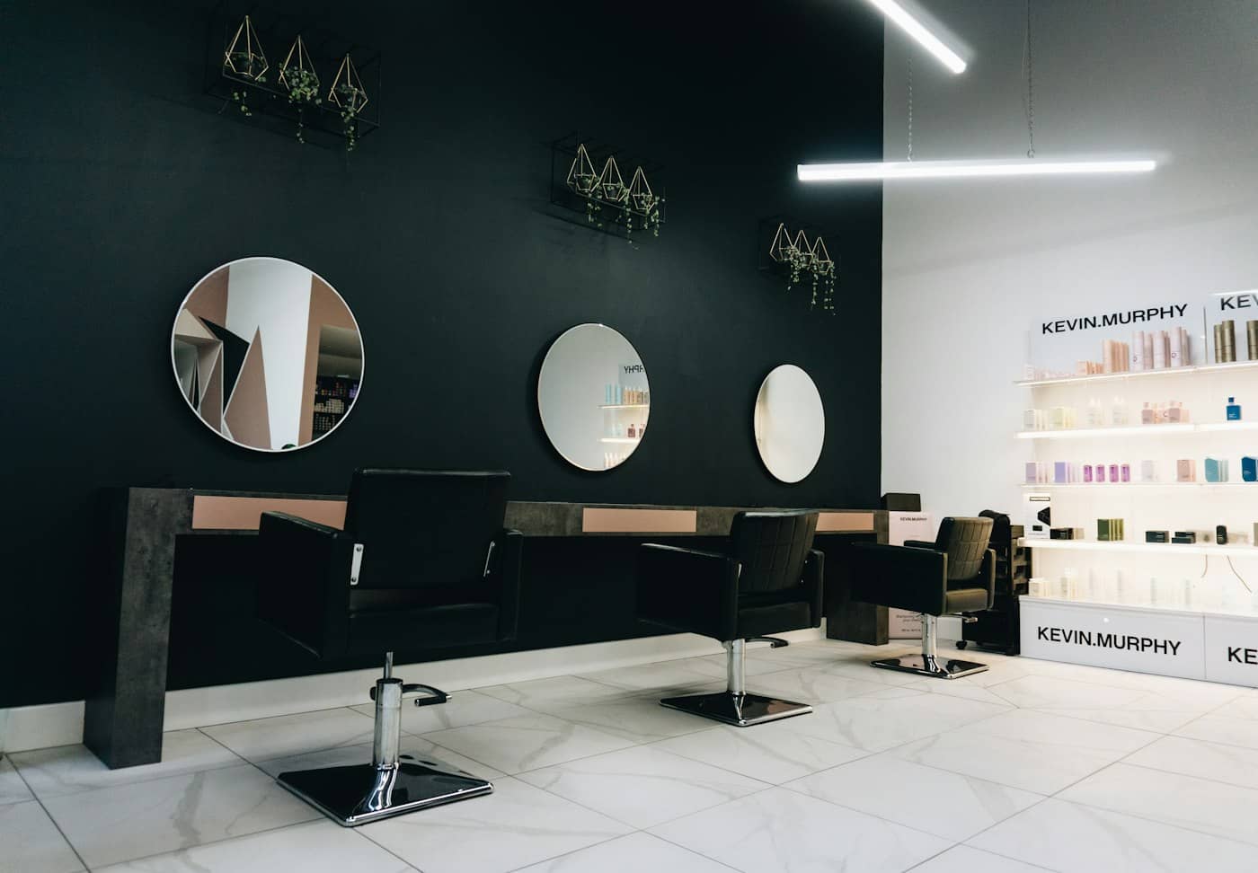 Salon de coiffure contemporain, fauteuils noirs face à des miroirs ronds